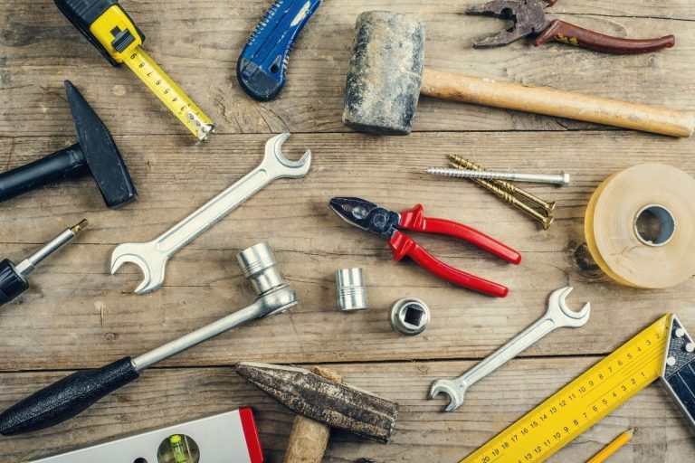 Different hand tools, such as a tape measure and screwdriver, laid out on a wooden table for easy access.